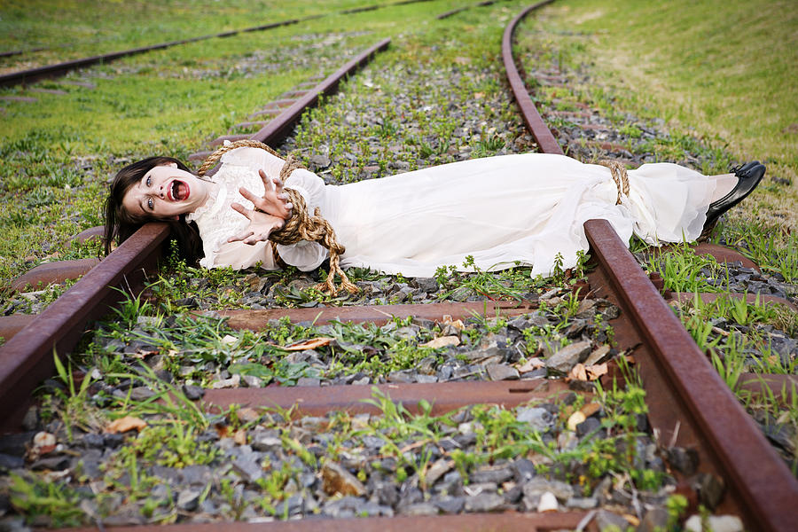Woman in period dress lies bound and screaming on railtrack Photograph by RapidEye