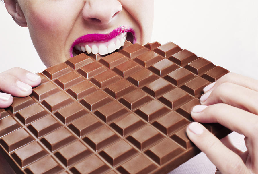 Woman in pink lipstick biting large chocolate bar Photograph by Chris Ryan