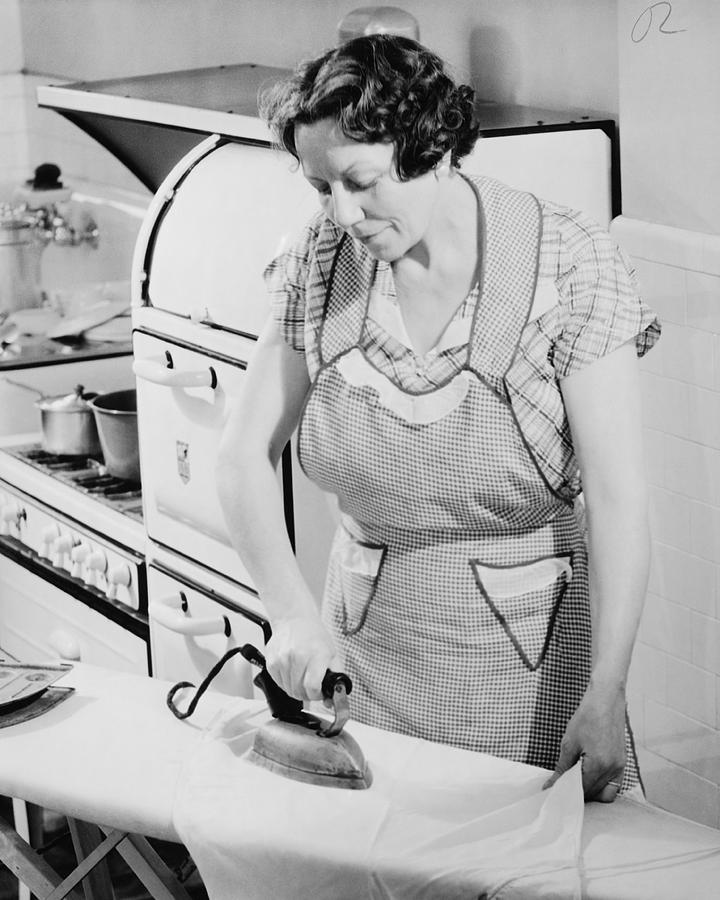 Woman ironing in kitchen, (B&W) Photograph by George Marks