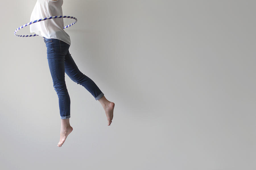 Woman jumping mid air with plastic hoop round her waist Photograph by Pchyburrs