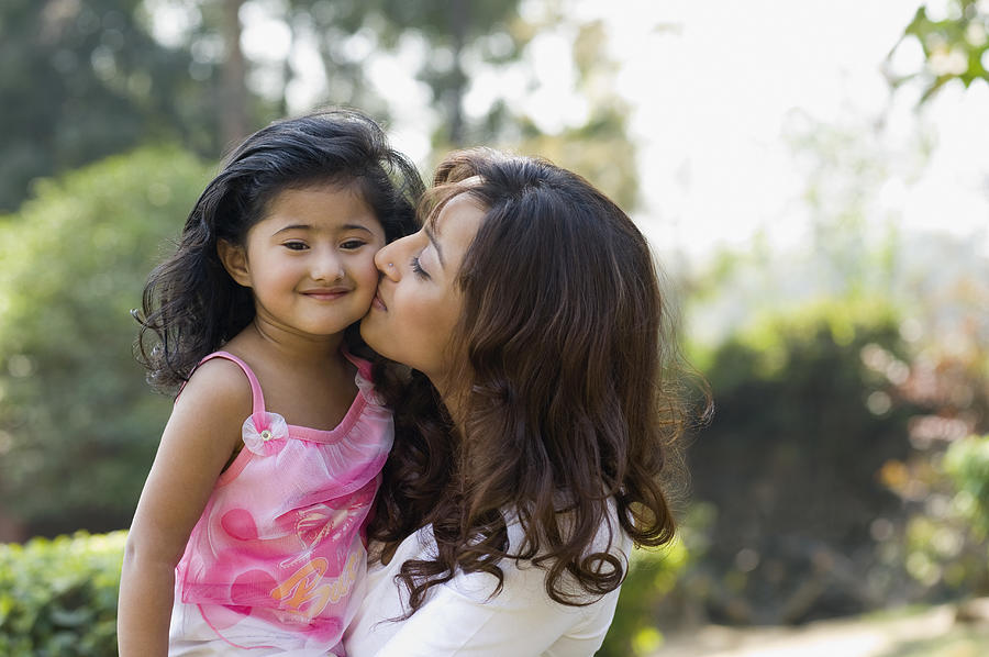 Woman kissing her daughter in a park Photograph by Photosindia