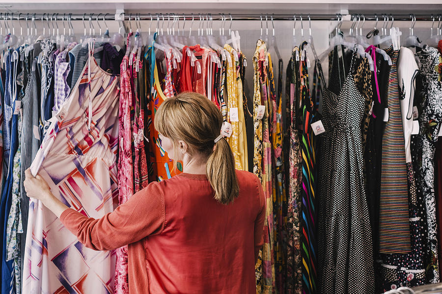 Woman looking at dress hanging on rack while standing at store Photograph by Maskot