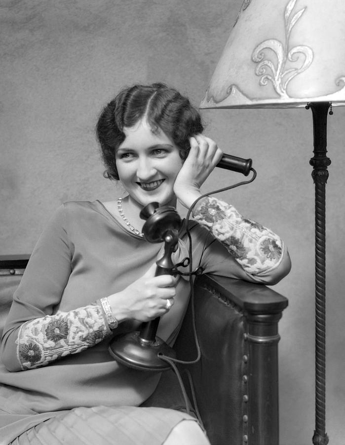 Woman On Candle Stick Phone Sitting On Couch By Lamp Smiling Flirting. Photograph by H. Armstrong Roberts