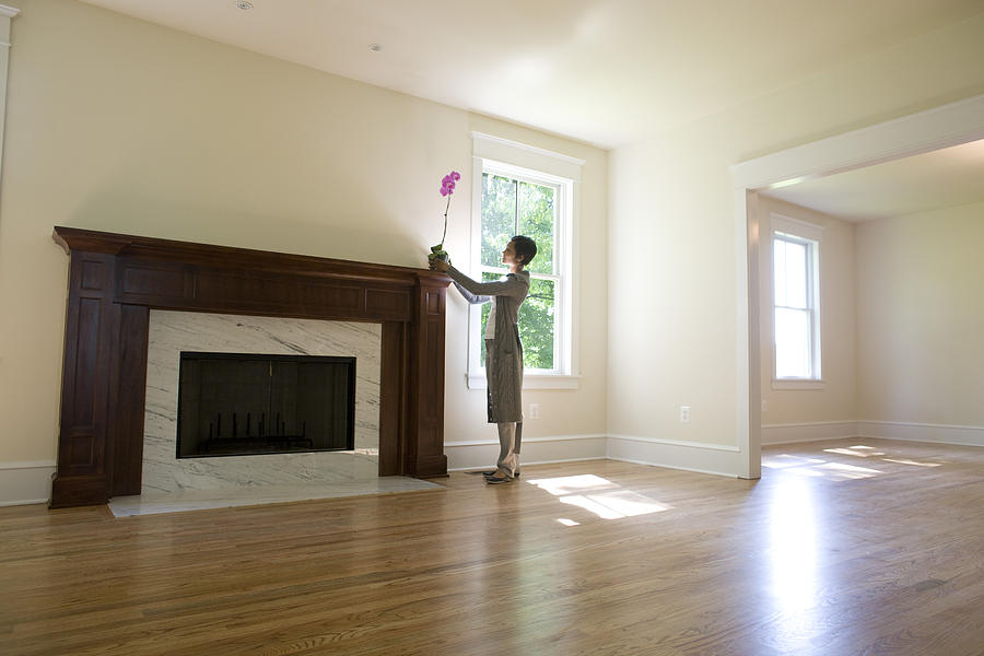 Woman placing orchid on fireplace in empty room Photograph by David Sacks