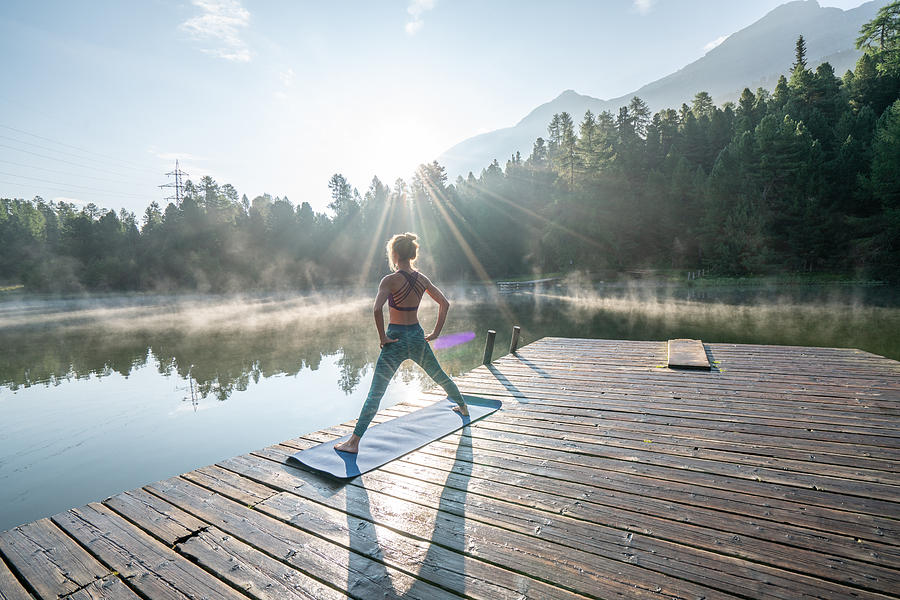 Woman practicing yoga poses in nature, lake pier Photograph by Swissmediavision