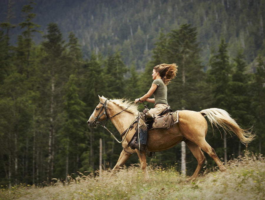 Woman riding horse through field.  Photograph by Thomas Northcut