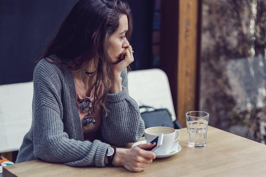 Woman sitting alone, having coffee and texting on her mobile phone Photograph by Mixmike