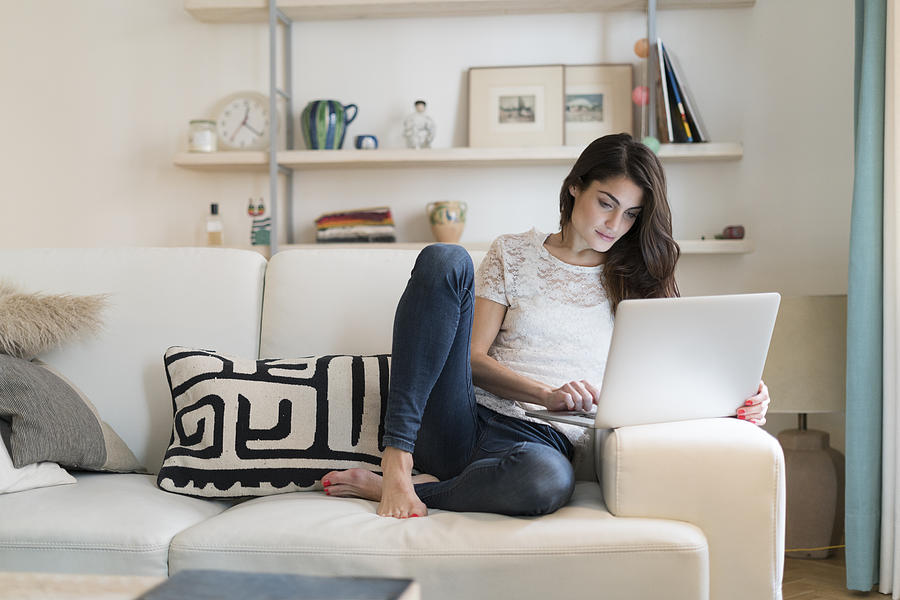 Woman sitting on couch at home using laptop Photograph by Westend61
