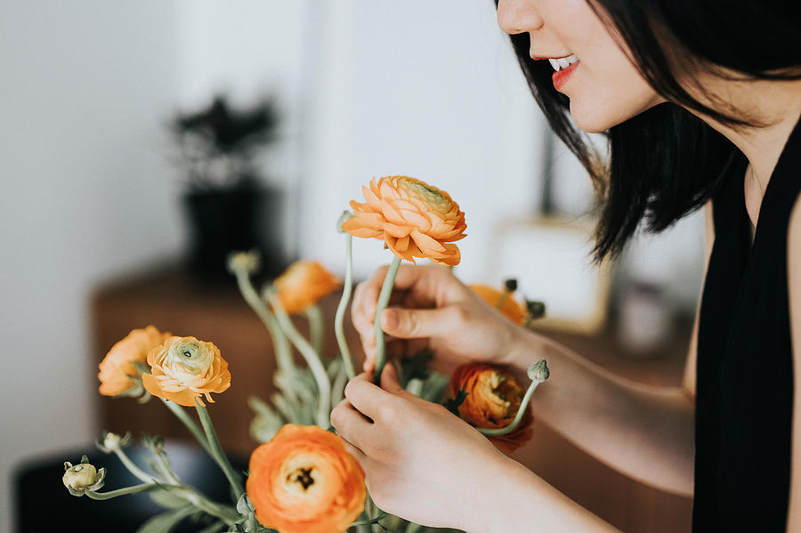 Woman smelling flowers while arranging it at home Photograph by D3sign
