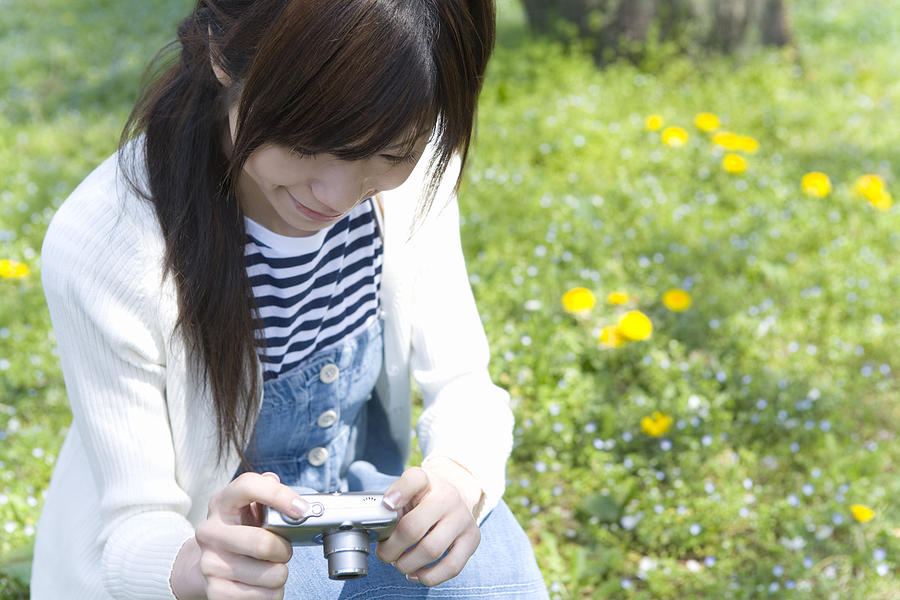 Woman smiling and holding a digital camera on lawn, front view, Japan Photograph by Daj