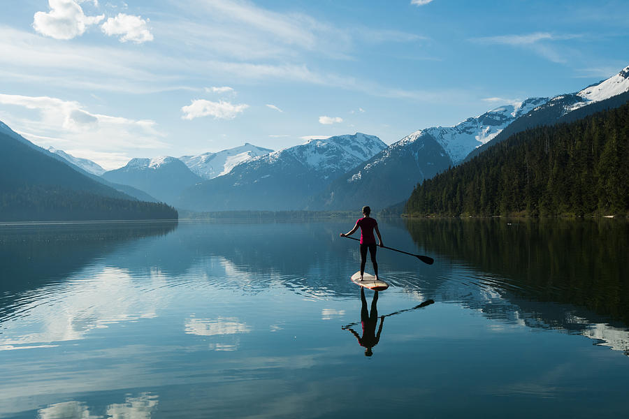 Woman stand up paddle boarding on a pristine mountain lake Photograph by stockstudioX Woman stand up paddle boarding on a pristine mountain lake Photograph by stockstudioX