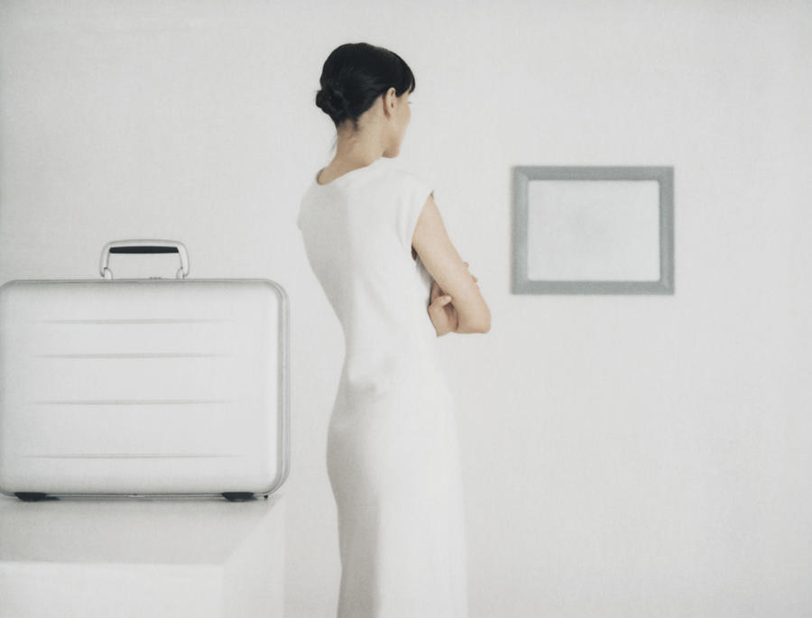 Woman standing next to table with metallic briefcase looking toward frame on wall Photograph by Matthieu Spohn