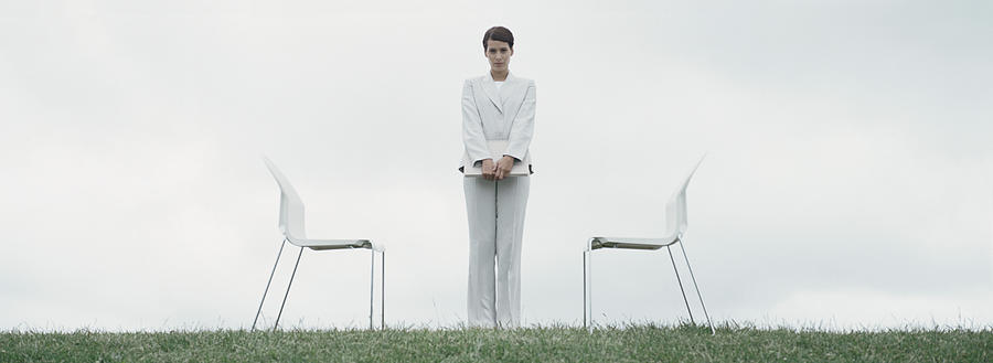Woman standing outdoors on grass between two chairs in front of overcast sky Photograph by Matthieu Spohn