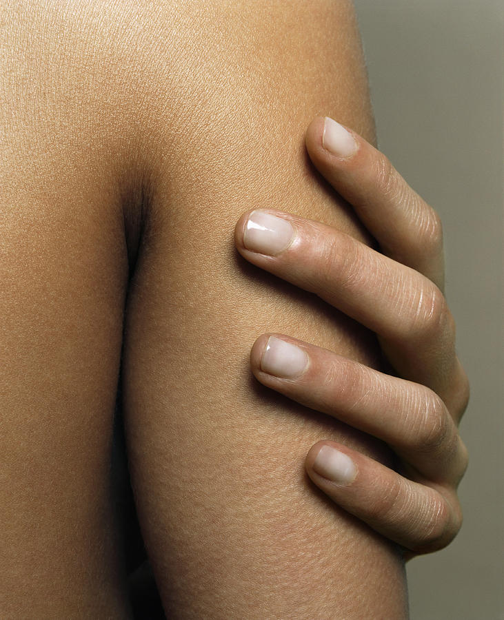 Woman touching arm, close-up Photograph by Andreas Kuehn