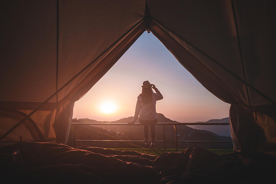 Woman traveler sitting outside camping tent and looking at sunrise view and mountain range.Travel outdoors camping for exploration and freedom concept. Photograph by Pojcheewin Yaprasert Photography