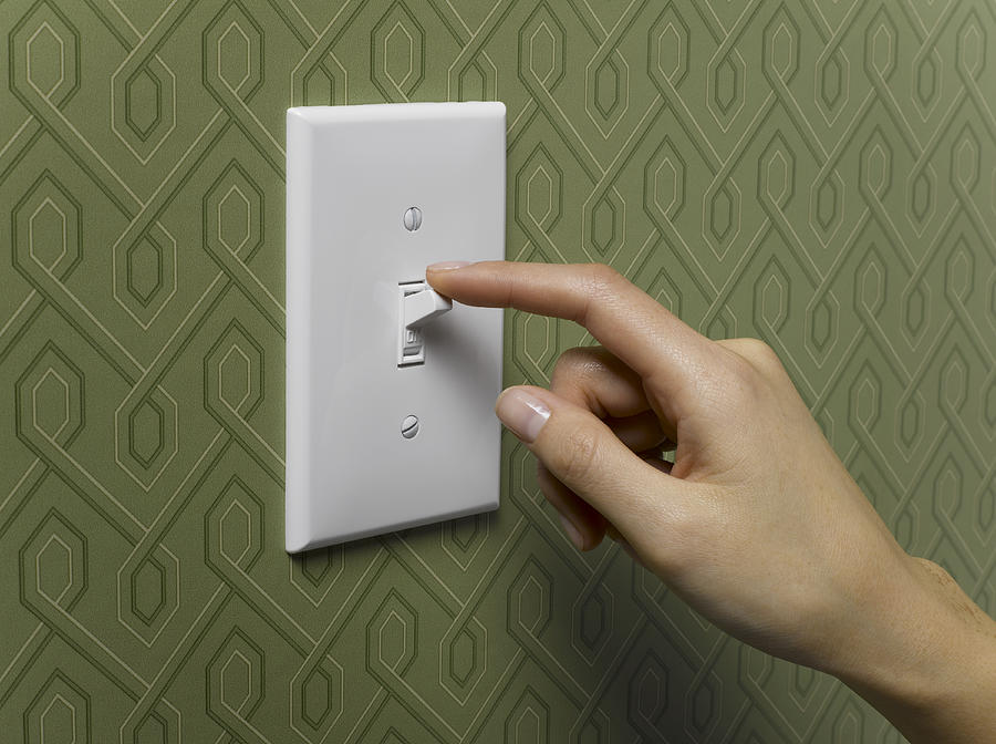 Woman turning off light switch on green wallpapered wall, close-up Photograph by Jeffrey Hamilton