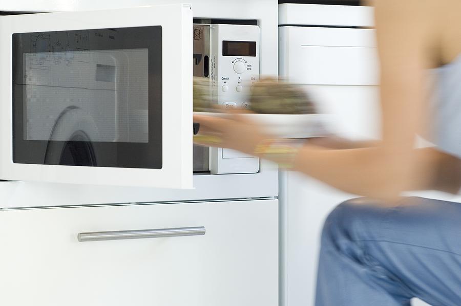 Woman using a microwave, close-up Photograph by Eric Audras