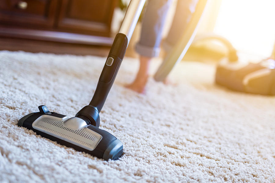 Woman using a vacuum cleaner while cleaning carpet in the house. Photograph by Scyther5