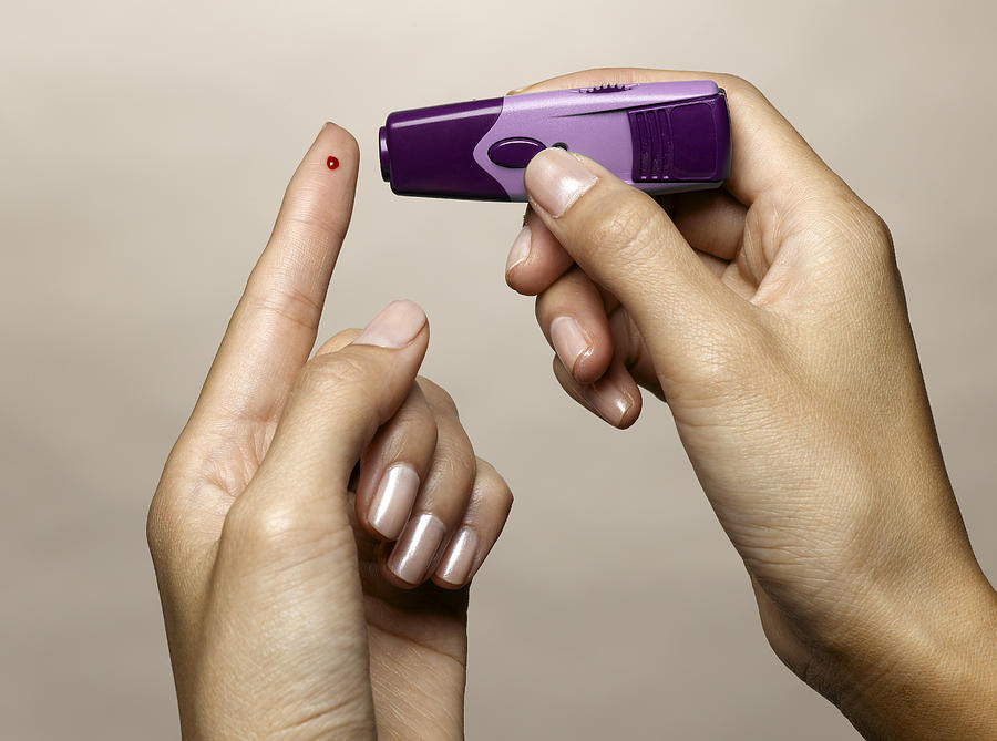 Woman using diabetes test kit Photograph by Jeffrey Hamilton