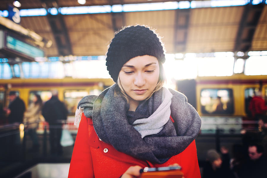 Woman using smartphone on a train station. Photograph by Guido Mieth
