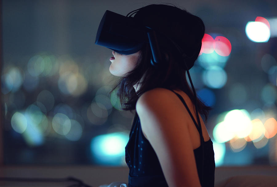 Woman using virtual reality headset at night with city lights in background Photograph by Benjamin Torode