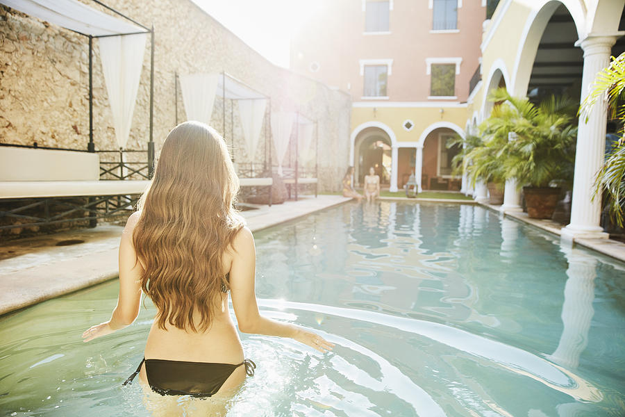 Woman wading into pool in courtyard of hotel while friends sit on edge Photograph by Thomas Barwick