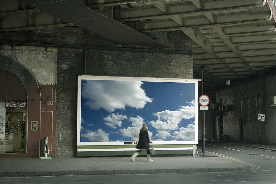 Woman walking past billboard poster of cloudy sky on city street Photograph by Travelpix Ltd