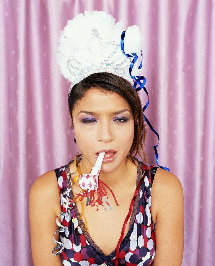 Woman wearing paper crown and blowing noisemaker, portrait Photograph by Thomas Barwick