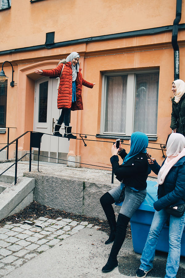 Woman with friends photographing female balancing on railing against building in city Photograph by Maskot