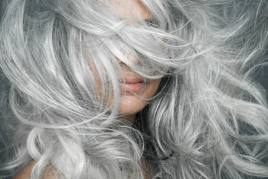 Woman with grey hair blowing across her face. Photograph by Andreas Kuehn