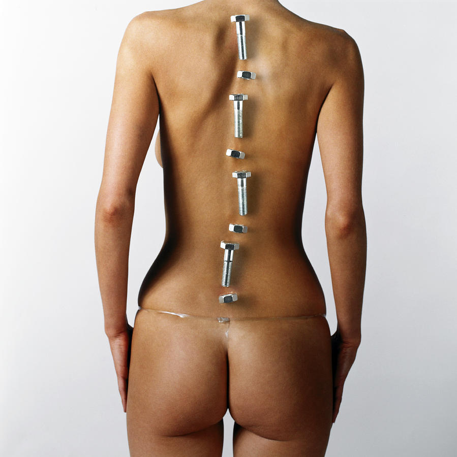 Woman with nuts and bolts placed over line of backbone, rear view Photograph by Adam Gault