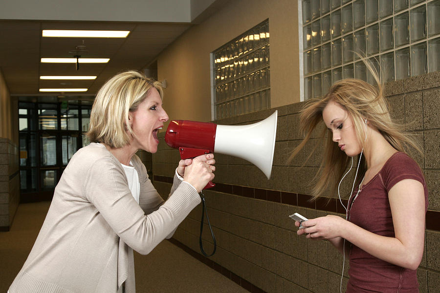 Woman yelling through a bullhorn at an unfazed teenage girl Photograph by Njgphoto