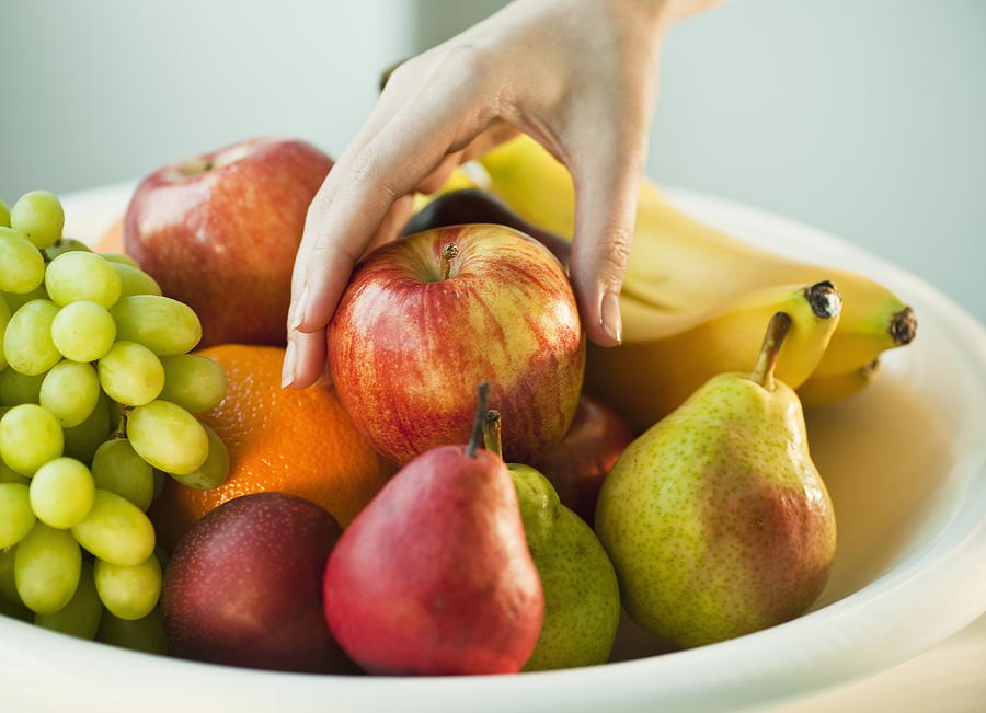 Womans hand taking apple from fruit bowl Photograph by Tetra Images