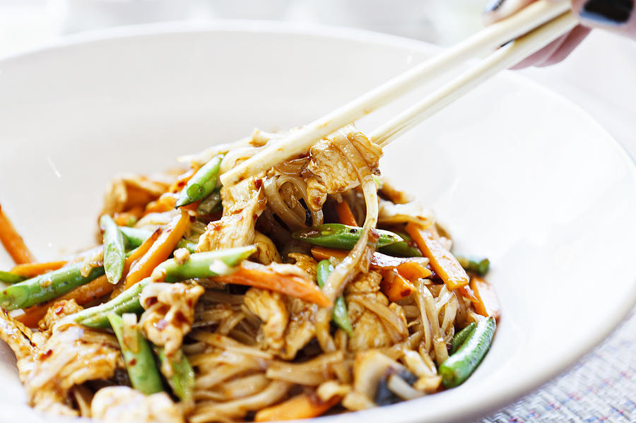Womans hand uses chopsticks to serve Thai chicken noodle dish Photograph by RapidEye
