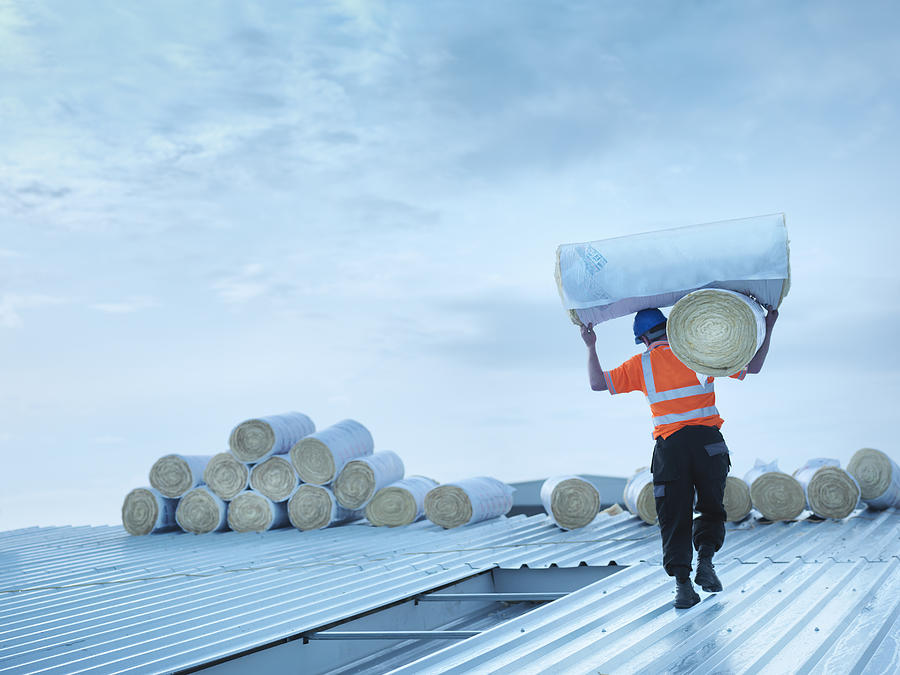 Worker carrying insulation on roof Photograph by Monty Rakusen