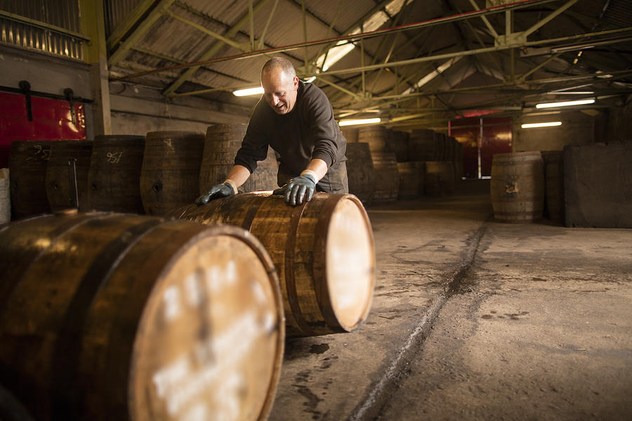 Worker rolling whisky cask in whisky distillery warehouse Photograph by Leon Harris