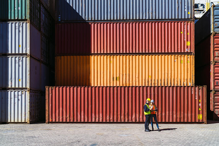 Workers having discussion against cargo containers Photograph by Portra