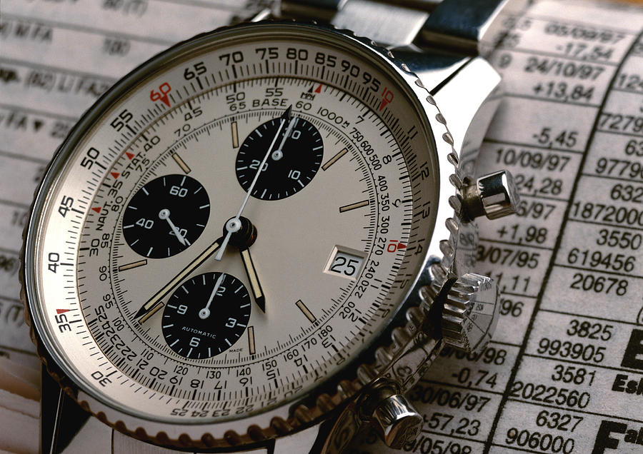 Wristwatch on top of stock report, extreme close-up Photograph by Christian Zachariasen