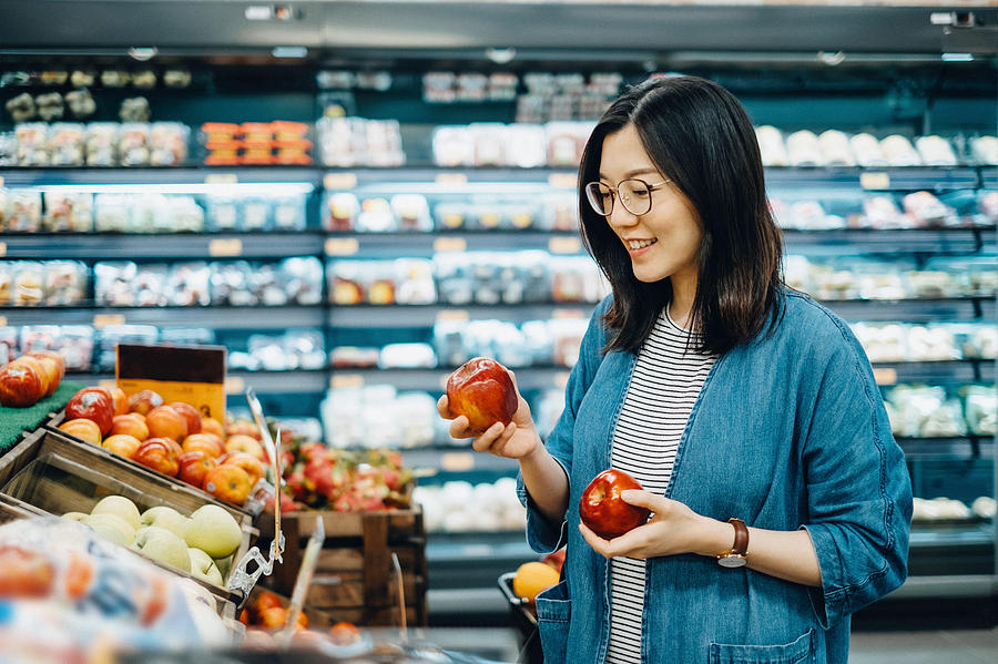 Young Asian woman shopping for fresh organic fruits in supermarket Photograph by D3sign