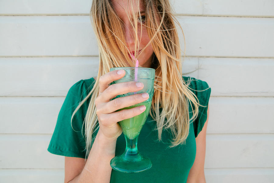 Young blond woman in a green top, drinking juice Photograph by Matilda Delves