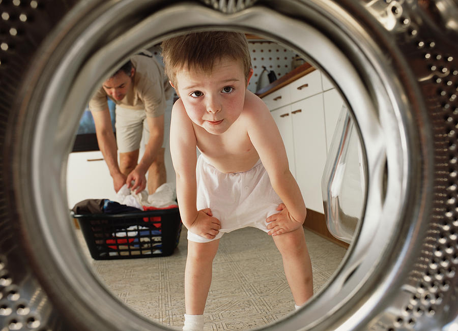 Young boy (4-6) looking inside washing machine,  father in background Photograph by Peter Cade