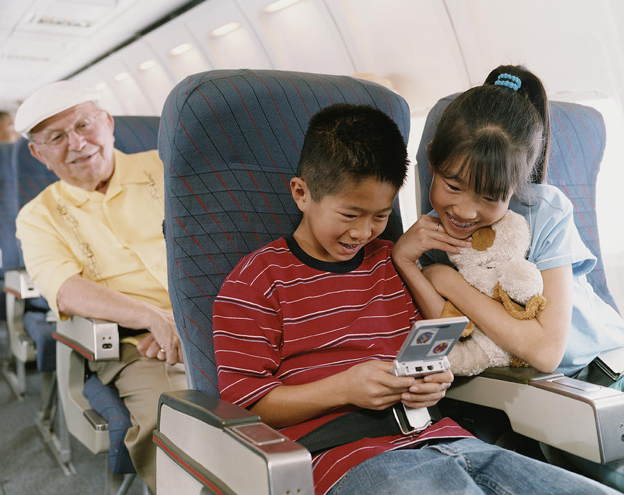 Young Boy and Girl Sit on a Plane Playing a Computer Game Photograph by Digital Vision.