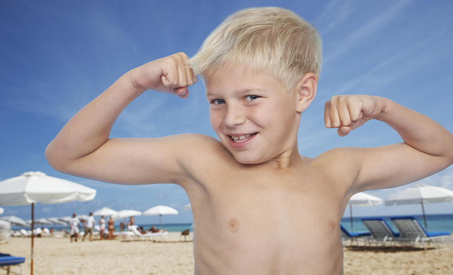 Young boy at the beach flexing biceps Photograph by Tom Merton