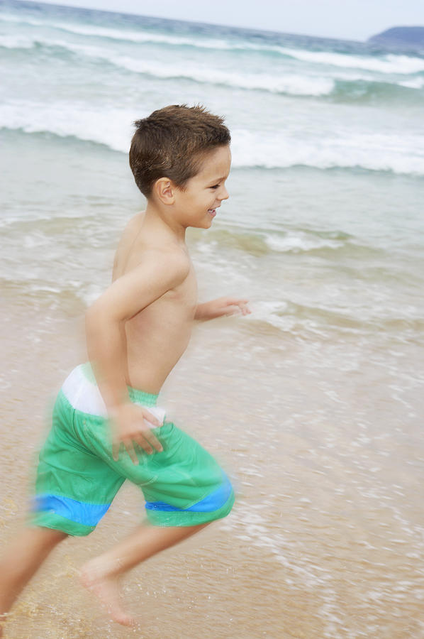 Young Boy in Swimming Trunks Runs By the Sea Photograph by Digital Vision.