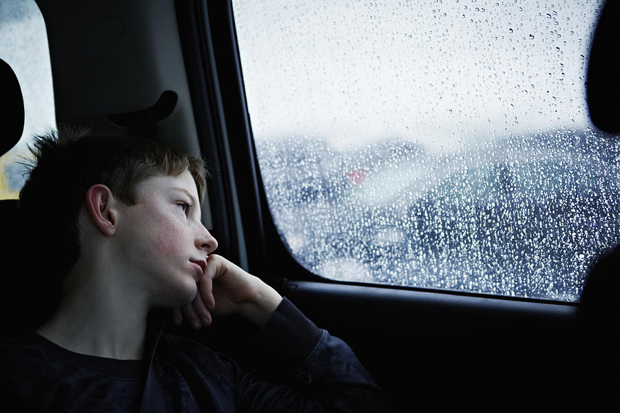Young boy looking out rainy car window Photograph by Thomas Barwick