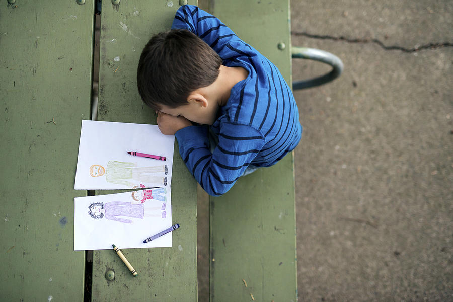Young boy looking sad at drawing of a broken family Photograph by FatCamera