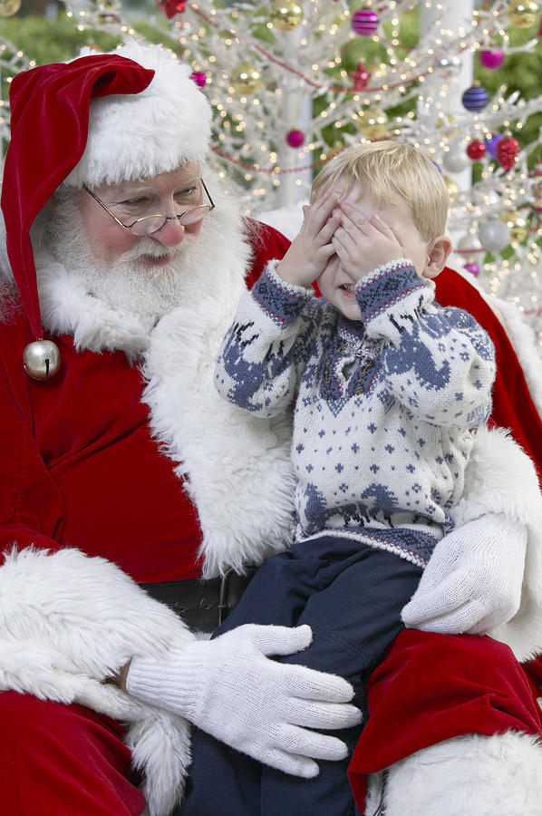 Young Boy Sitting on Father Christmas Lap With His Hand Over His Eyes Photograph by Digital Vision.