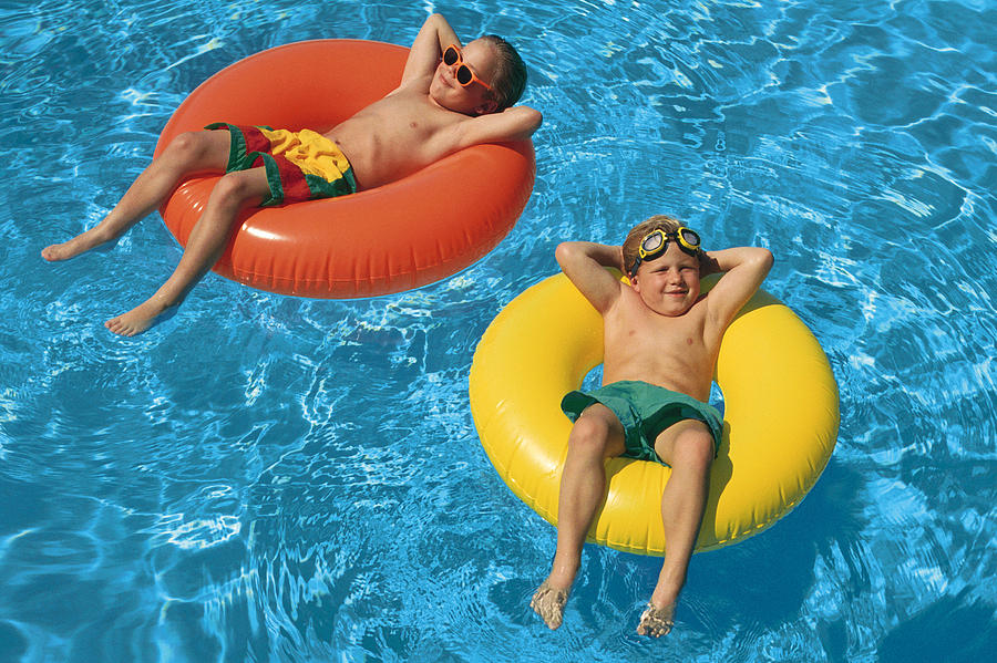 Young boys floating in inner tubes in swimming pool Photograph by Comstock