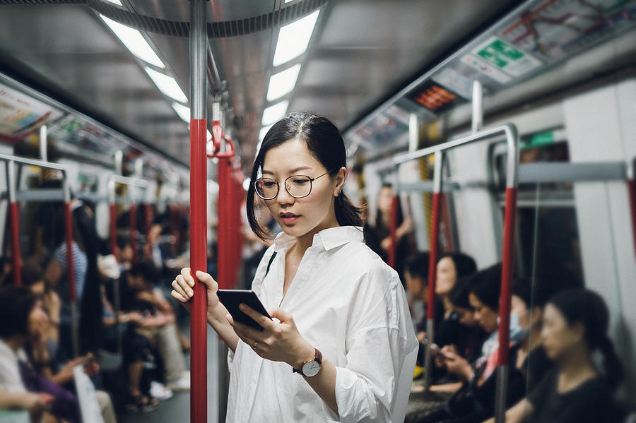 Young businesswoman looking at smartphone while riding on subway Photograph by D3sign