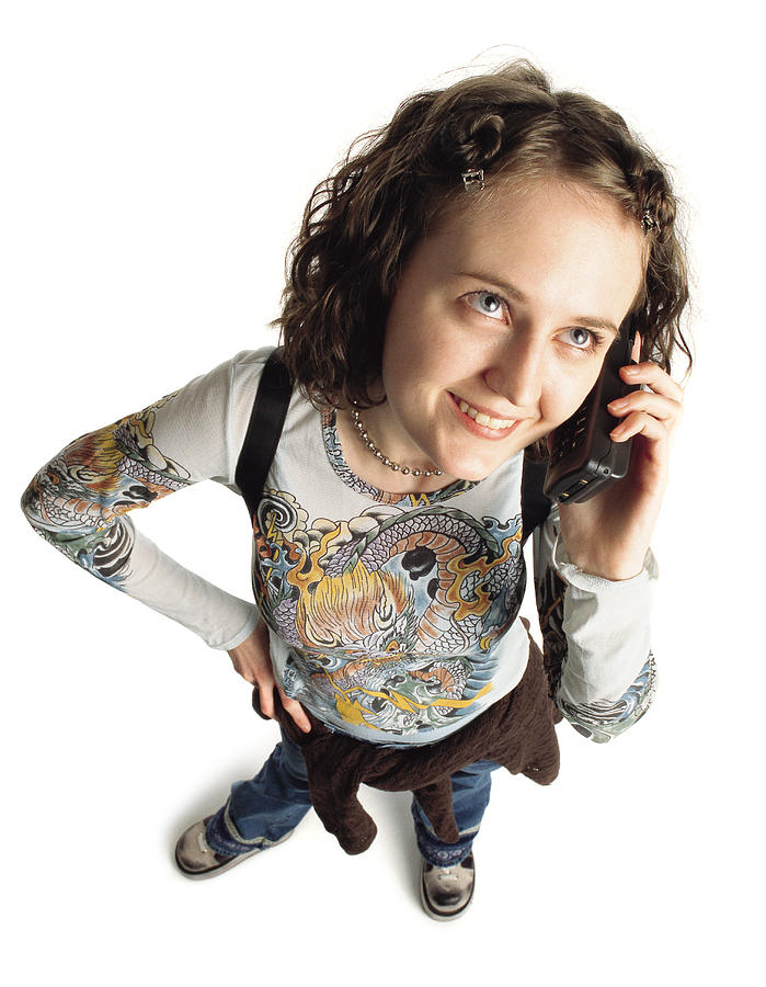 Young Caucasian Girl Student With Funky Hair Wearing A Shirt With A Dragon Painted On The Front A Sweatshirt Around Her Waist And Blue Pants Carries A Backpack And Talks On A Cellular Phone Photograph by Photodisc